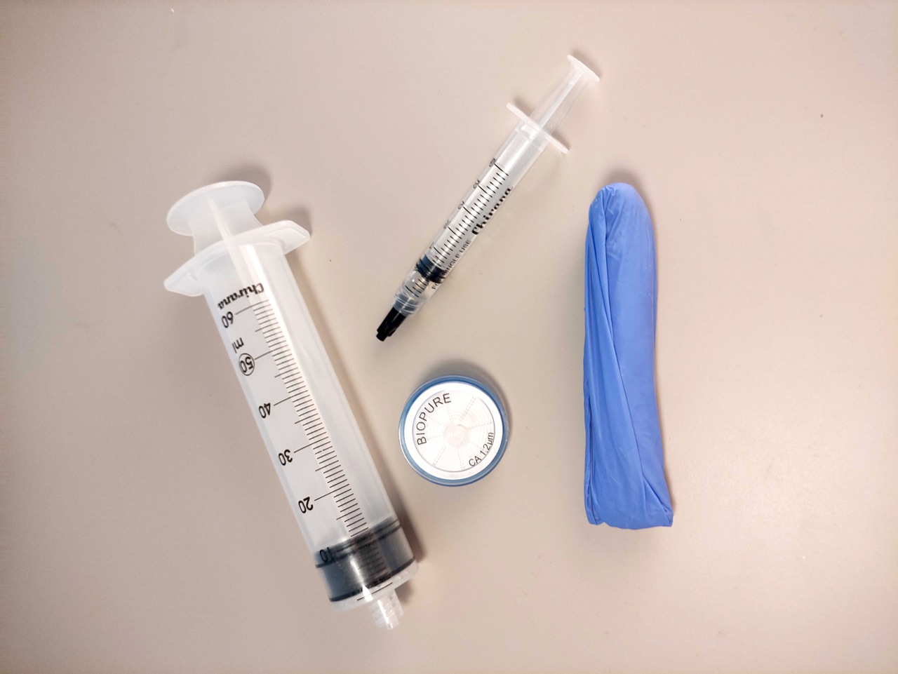 The contents of an eDNA Expeditions sampling kit laid out: a syringe, a disc filter, a preservation syringe, and a glove